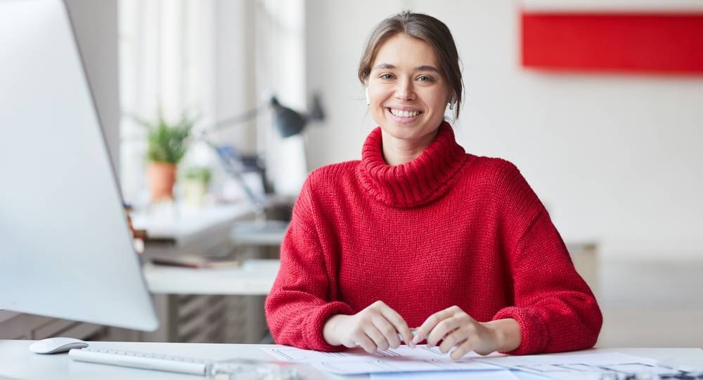 Žena ve svetru sedí u stolu s počítačem