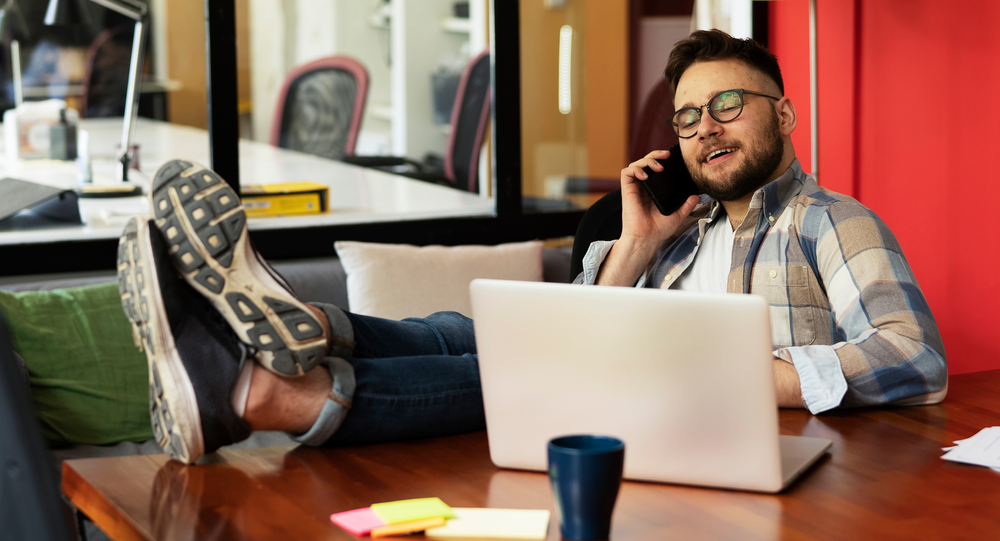 Muž v brýlích telefonuje s opřenýma nohama o stůl